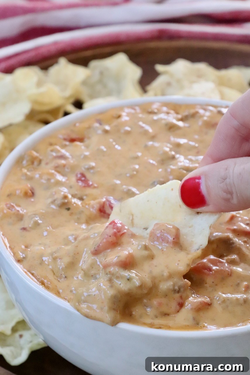 hand dipping a tortilla chip into rotel dip in a bowl