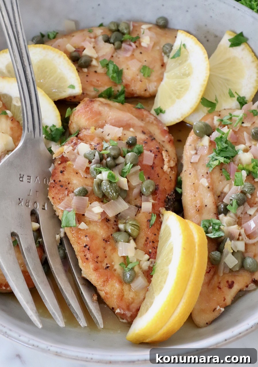 chicken piccata in a bowl with lemon wedges and a serving fork