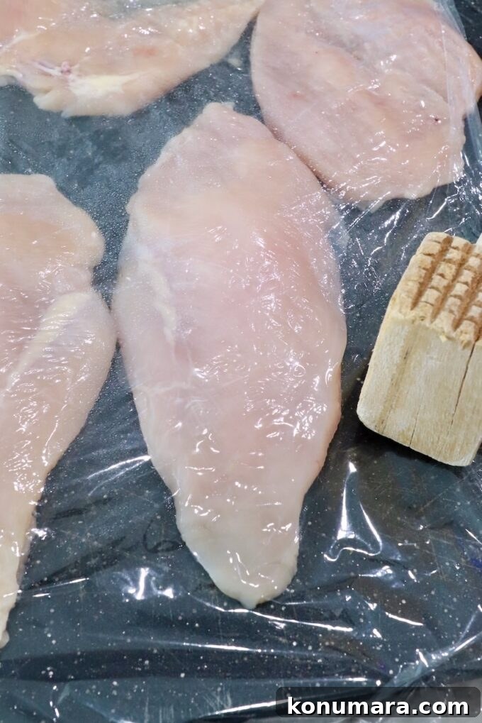 chicken breasts under plastic wrap on a cutting board
