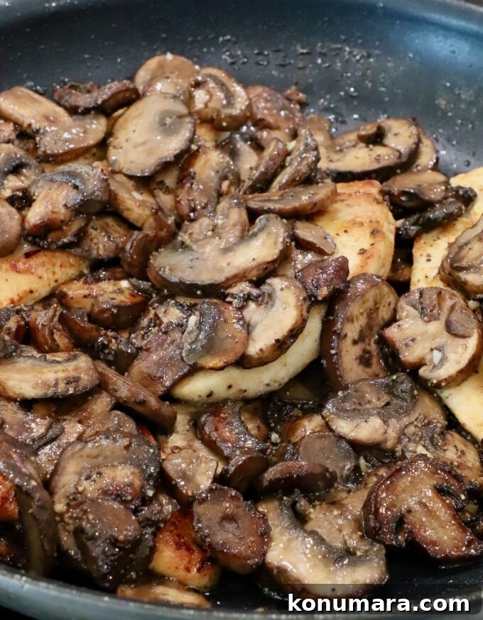 Pan Seared Chicken with Mushrooms and Swiss Cheese 9 sauteed mushrooms on top of chicken breasts in a skillet