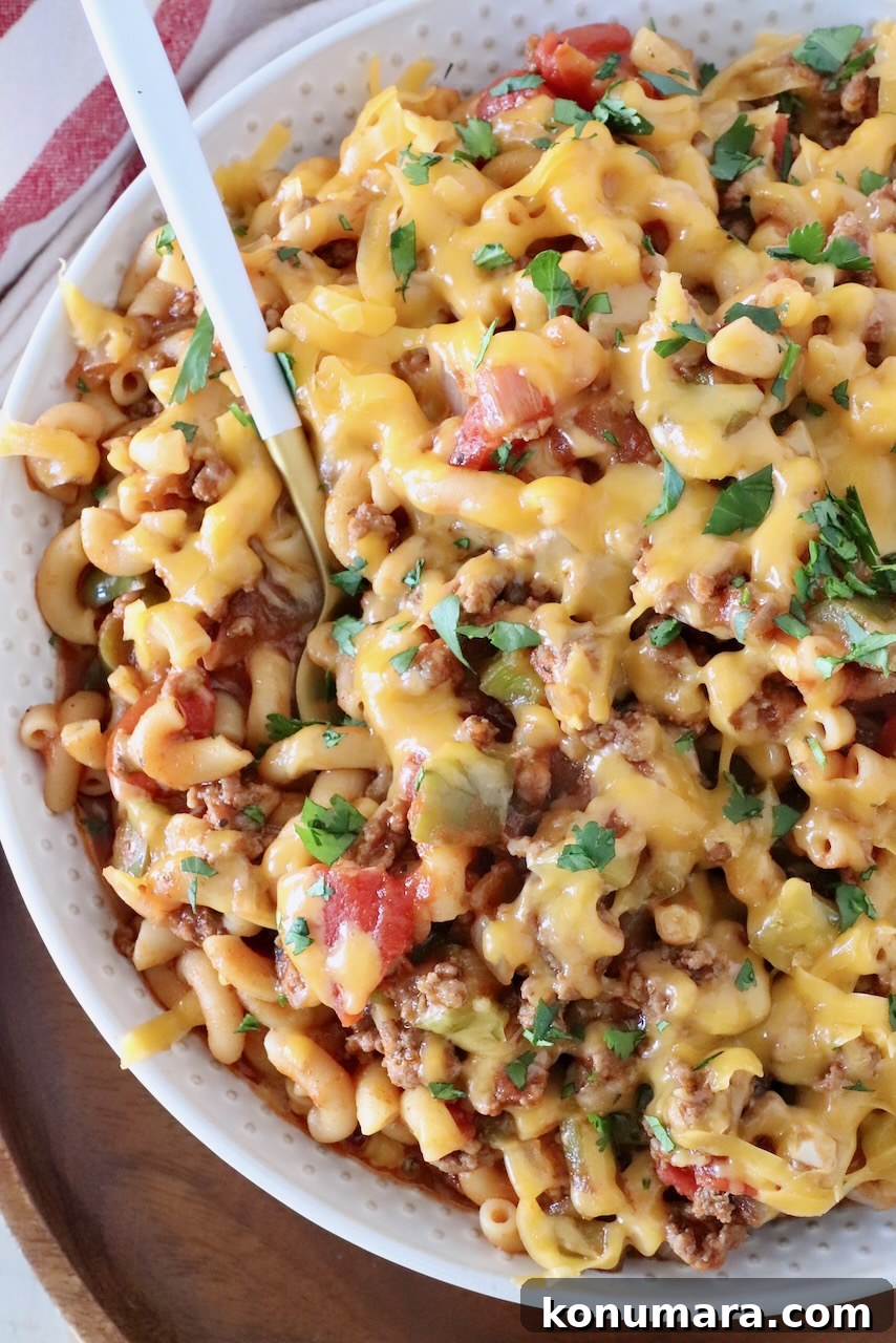 prepared goulash in a bowl with a spoon, covered with shredded cheddar cheese