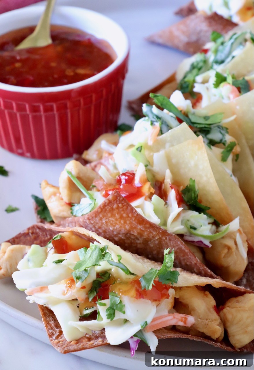 Wonton tacos filled with chicken and coleslaw lined up on a plate next to a small bowl of sweet chili sauce