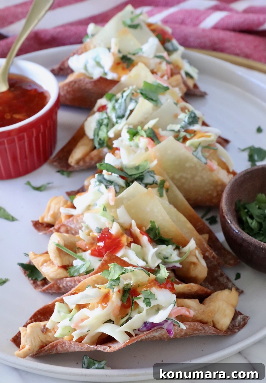 Wonton tacos filled with chicken and coleslaw on a plate next to a bowl of sweet chili sauce