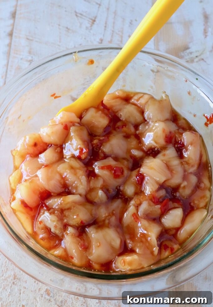 Diced chicken mixed with sweet chili sauce in a glass bowl with a yellow spatula