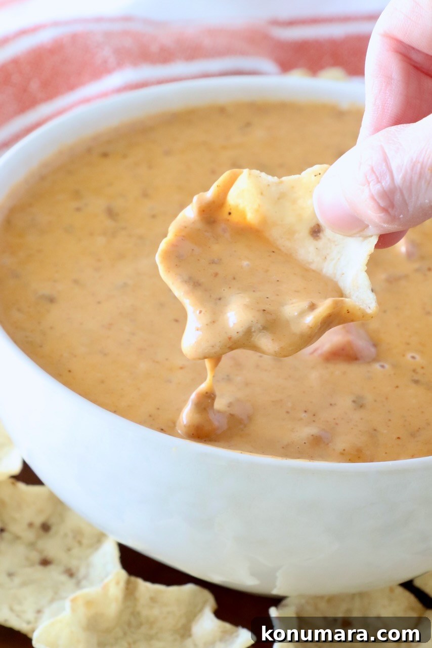 Creamy Chili Cheese Dip Recipe for Game Day 2 hand dipping a chip into prepared chili cheese dip in a bowl