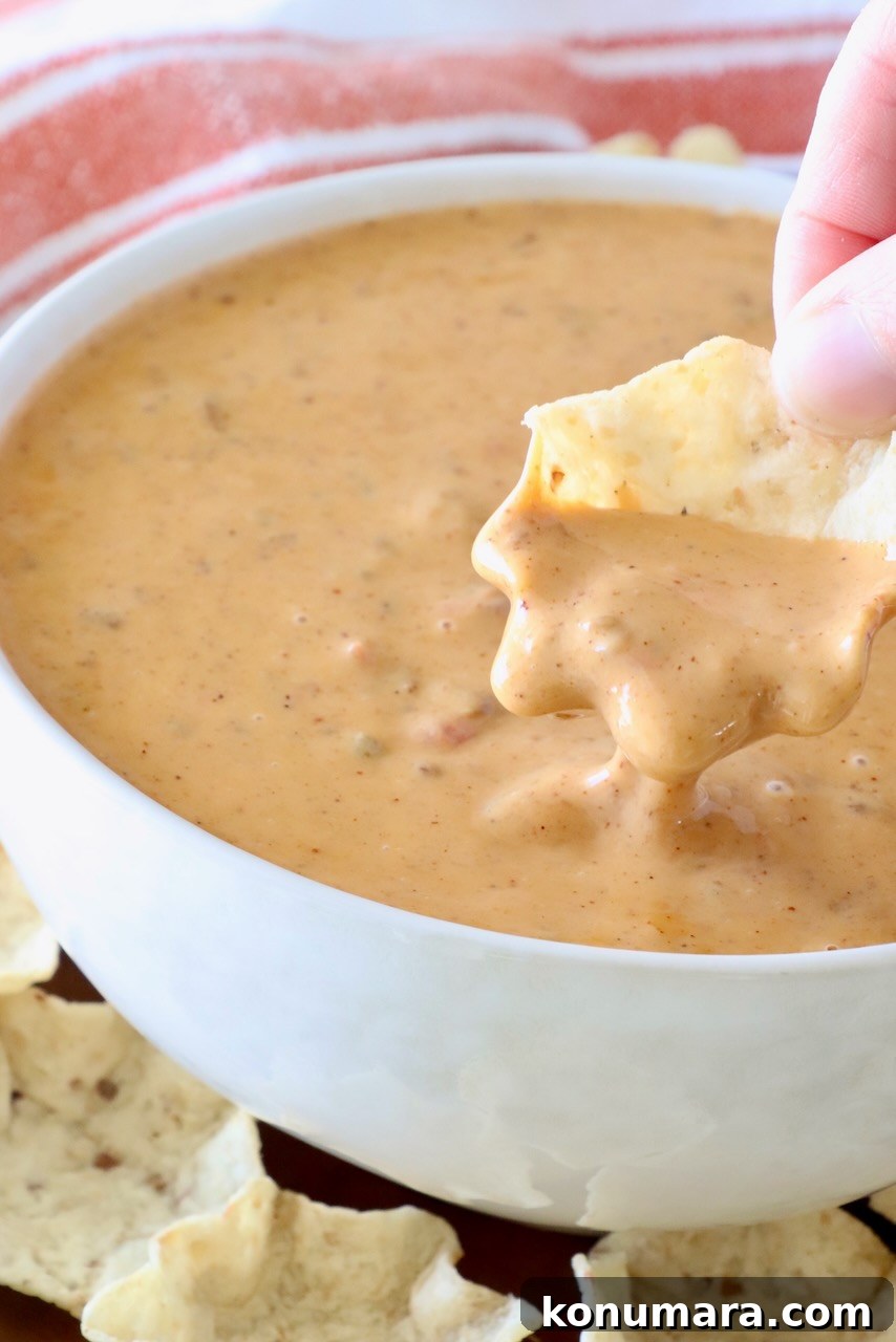 Creamy Chili Cheese Dip Recipe for Game Day 7 hand dipping a tortilla chip in a bowl of chili cheese dip