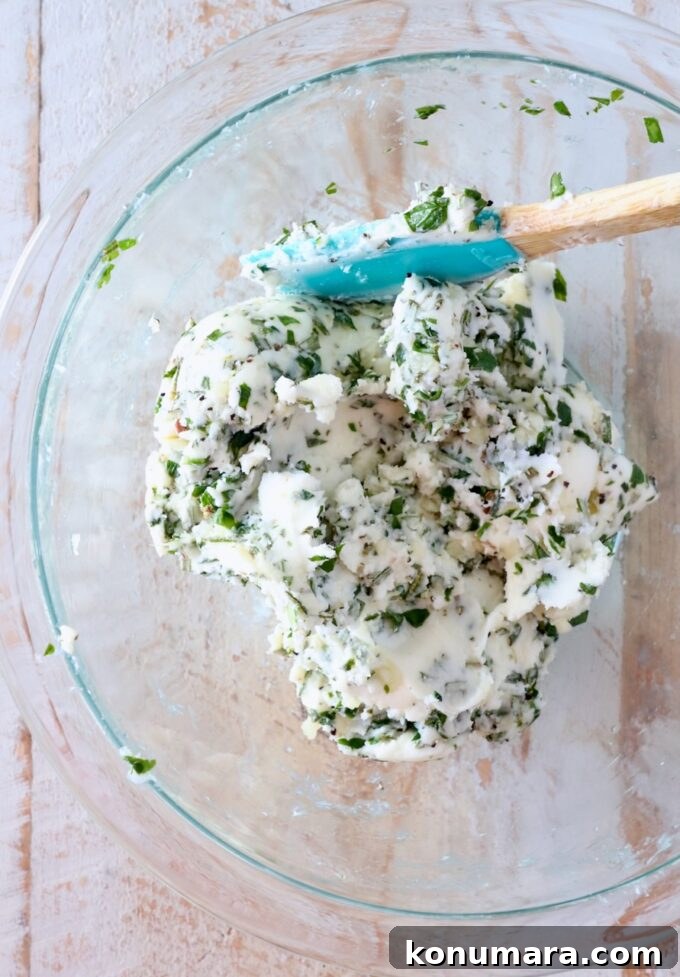 7 Homemade Compound Butter Recipes for Bread, Steak, and Veggies 5 garlic herb compound butter mixed together in a glass bowl with a spatula
