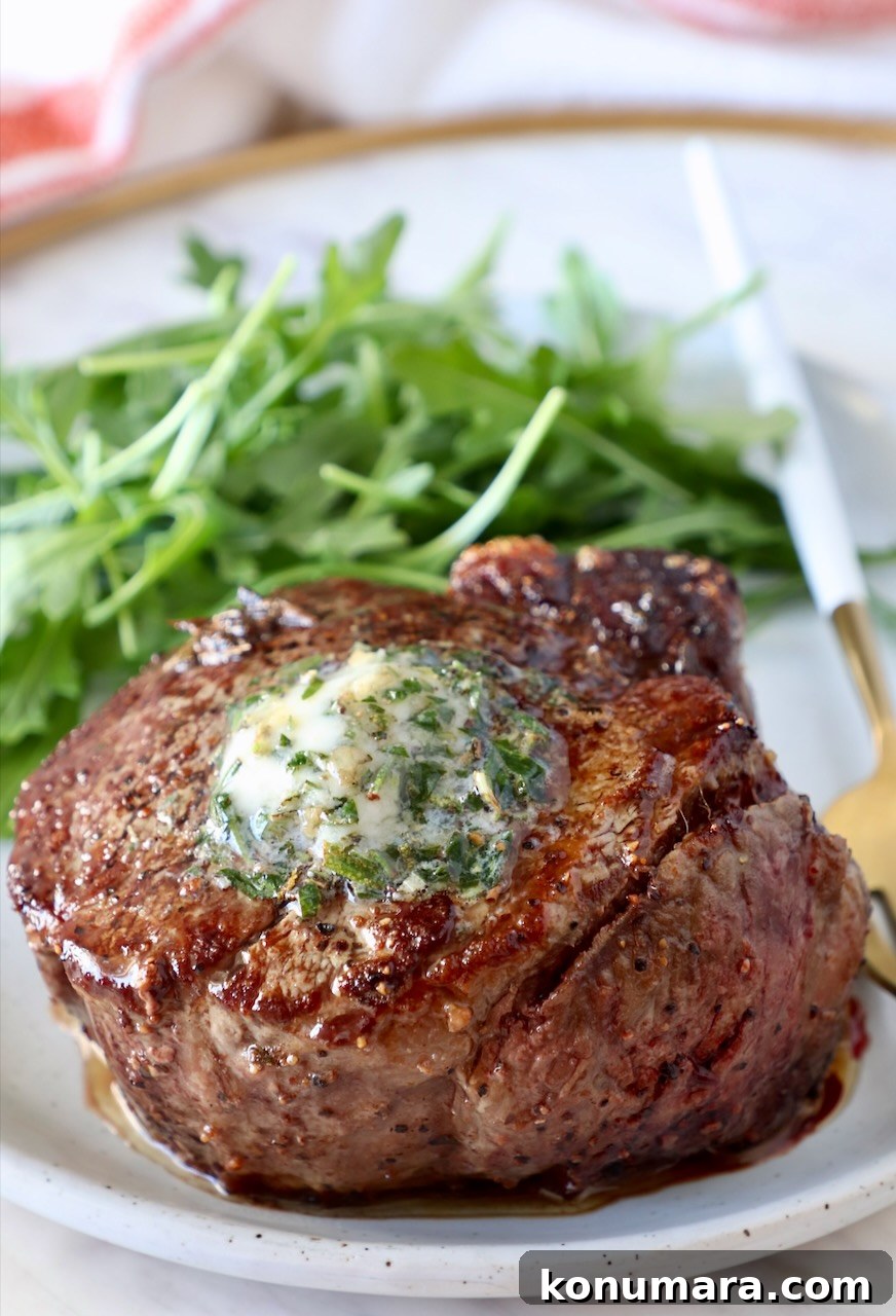 cooked steak on a plate topped with herb butter with arugula on the side of the plate