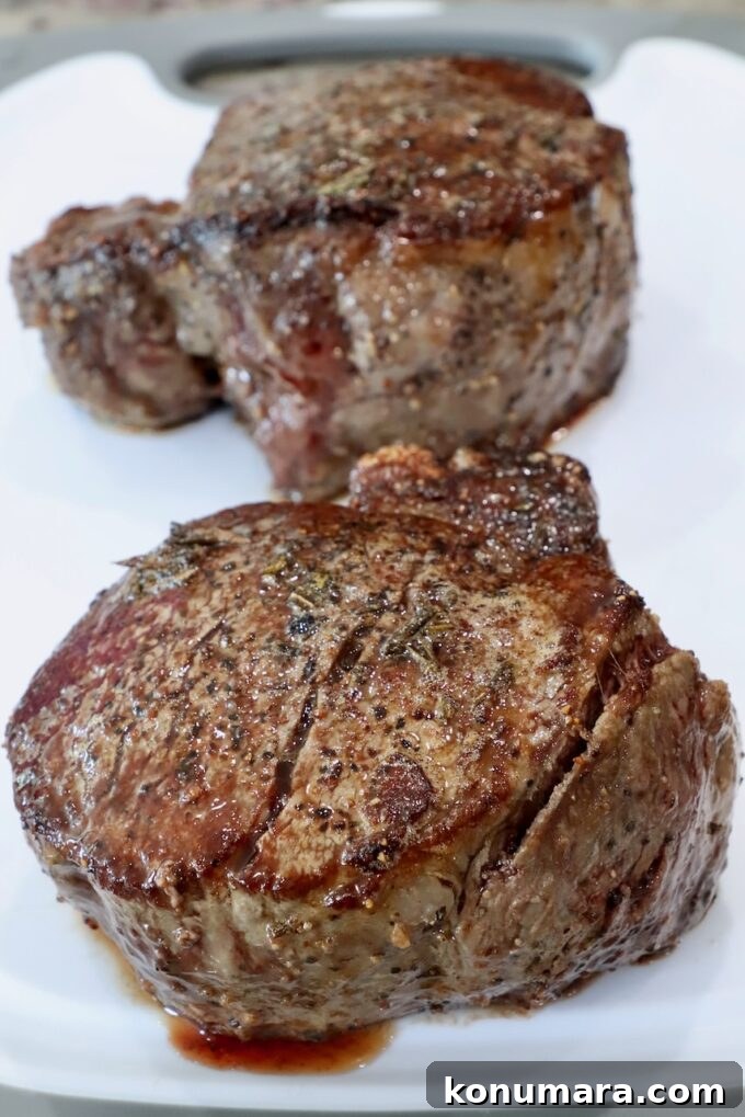 two cooked filet mignon steaks resting on a white cutting board