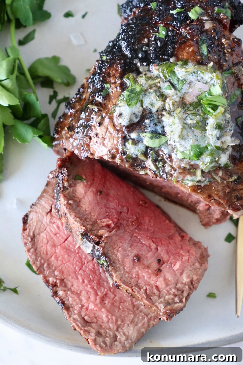 sliced, grilled filet mignon on a plate, topped with melted herb butter