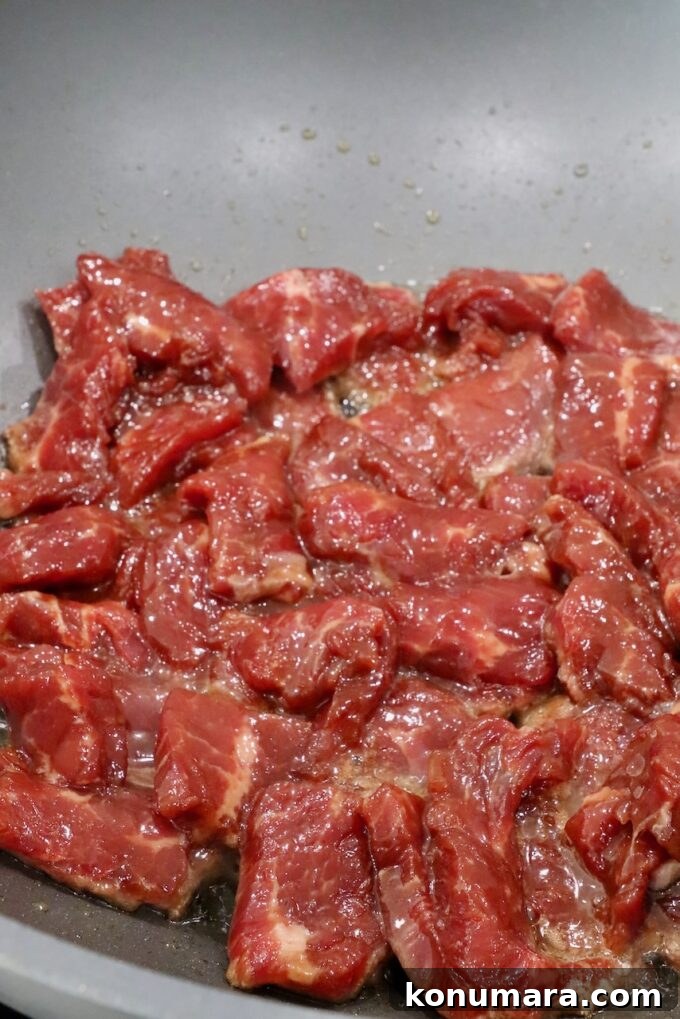Pepper Steak Stir-Fry Recipe with Bell Peppers 7 marinated strips of uncooked beef in a wok