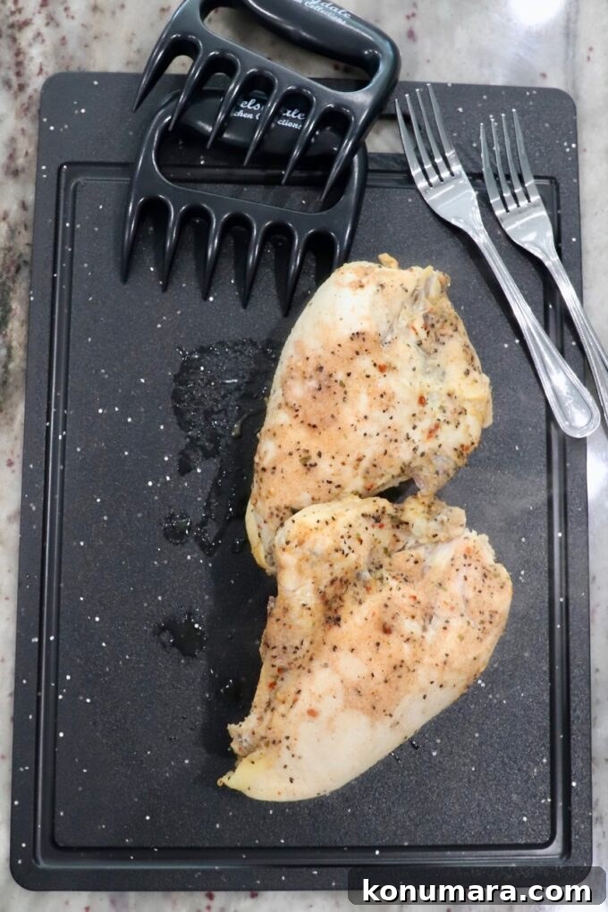 Slow Cooker Shredded Chicken Recipe for Tacos and Sandwiches 6 seasoned cooked chicken breasts on a cutting board with forks and meat claws on the side