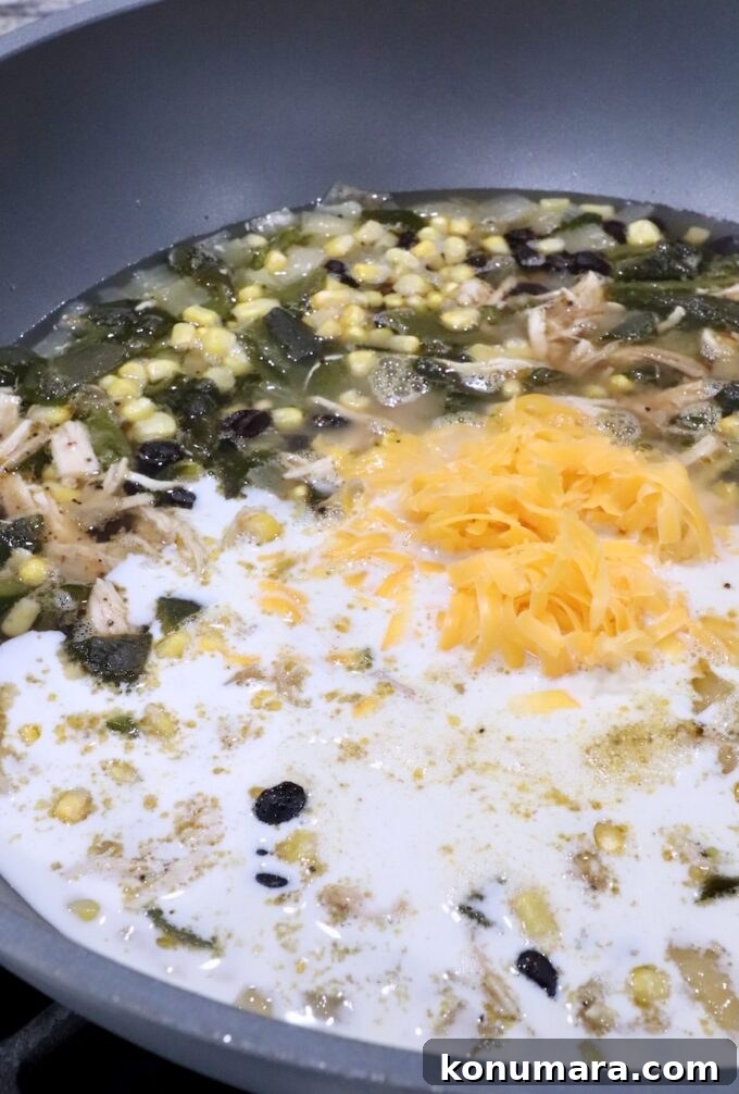 chicken poblano soup in a large pot with shredded cheddar cheese and heavy cream