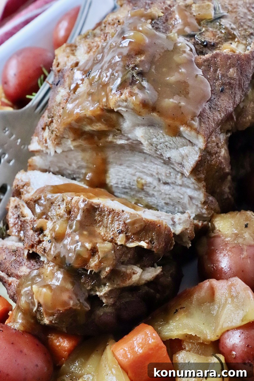 cooked pork roast, partially sliced on a large platter with roasted vegetables and gravy drizzled on top