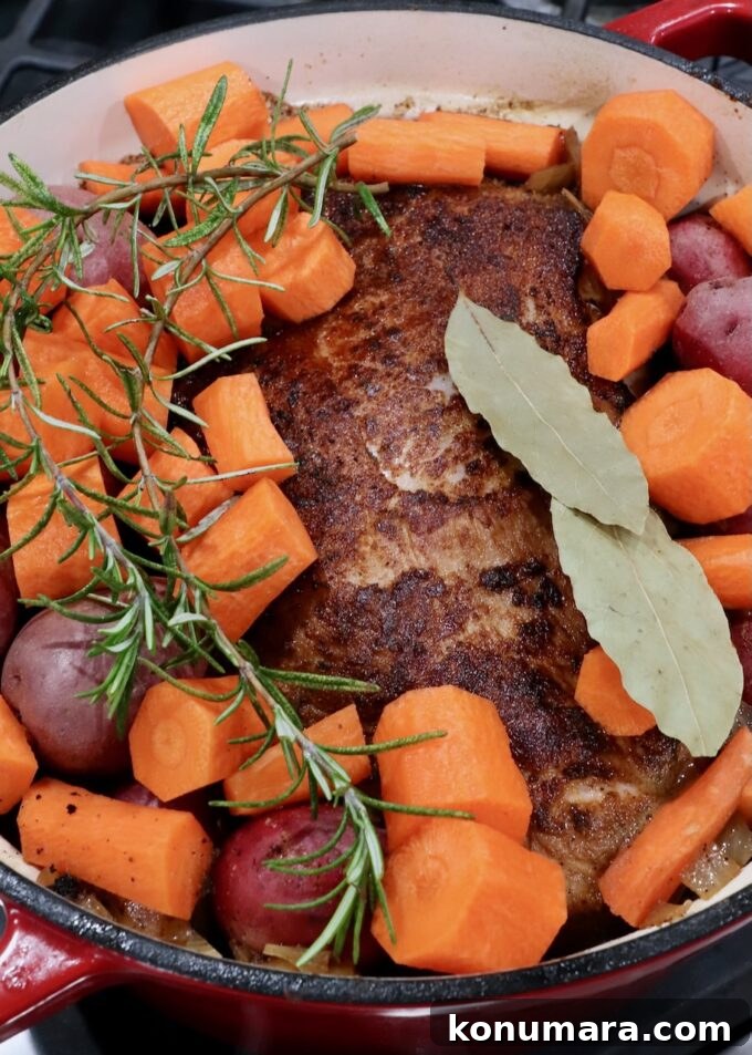 seared pork shoulder in a large pot with diced carrots, potatoes, bay leaves and rosemary