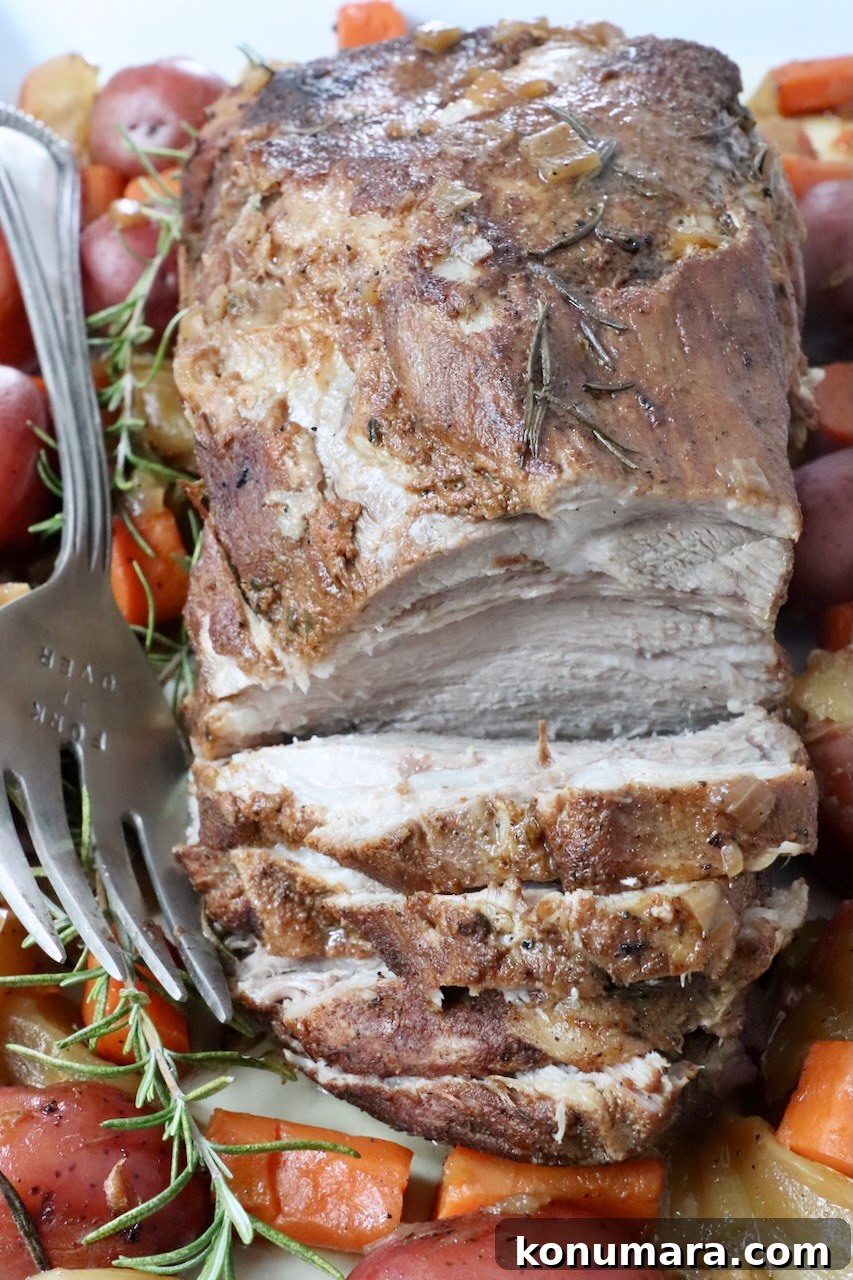 pork roast partially sliced on a serving plate with a large fork and roasted vegetables