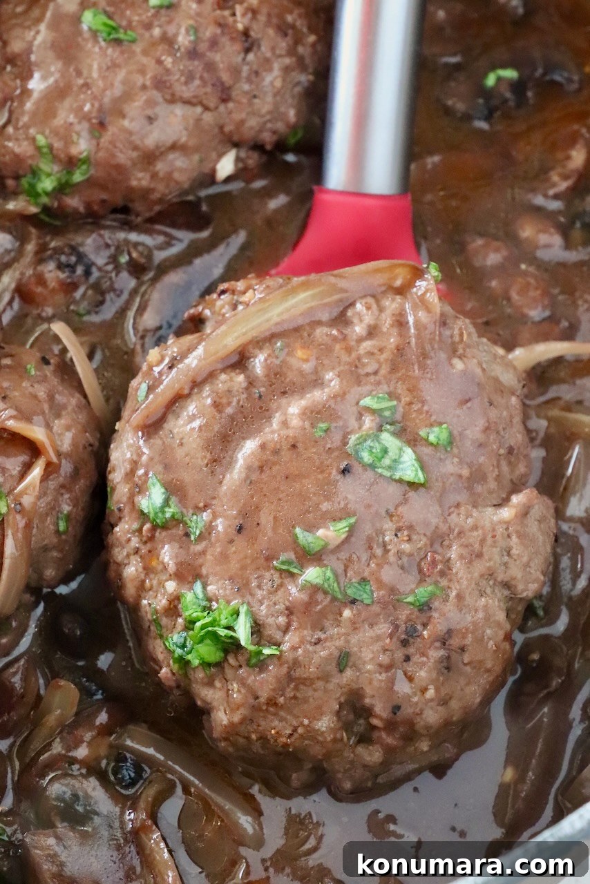 How to Make Chopped Steak with Mushroom Gravy 15 chopped steak in gravy in a pan with a red spatula