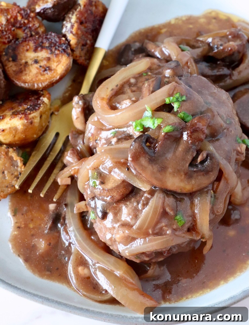 How to Make Chopped Steak with Mushroom Gravy 16 chopped steak on a plate with a fork covered with cooked sliced onions and mushrooms and gravy