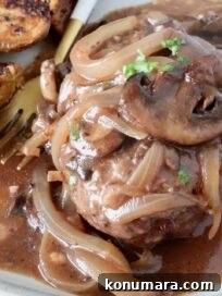 cooked chopped steak on a plate, covered with cooked, sliced onions and mushrooms and gravy