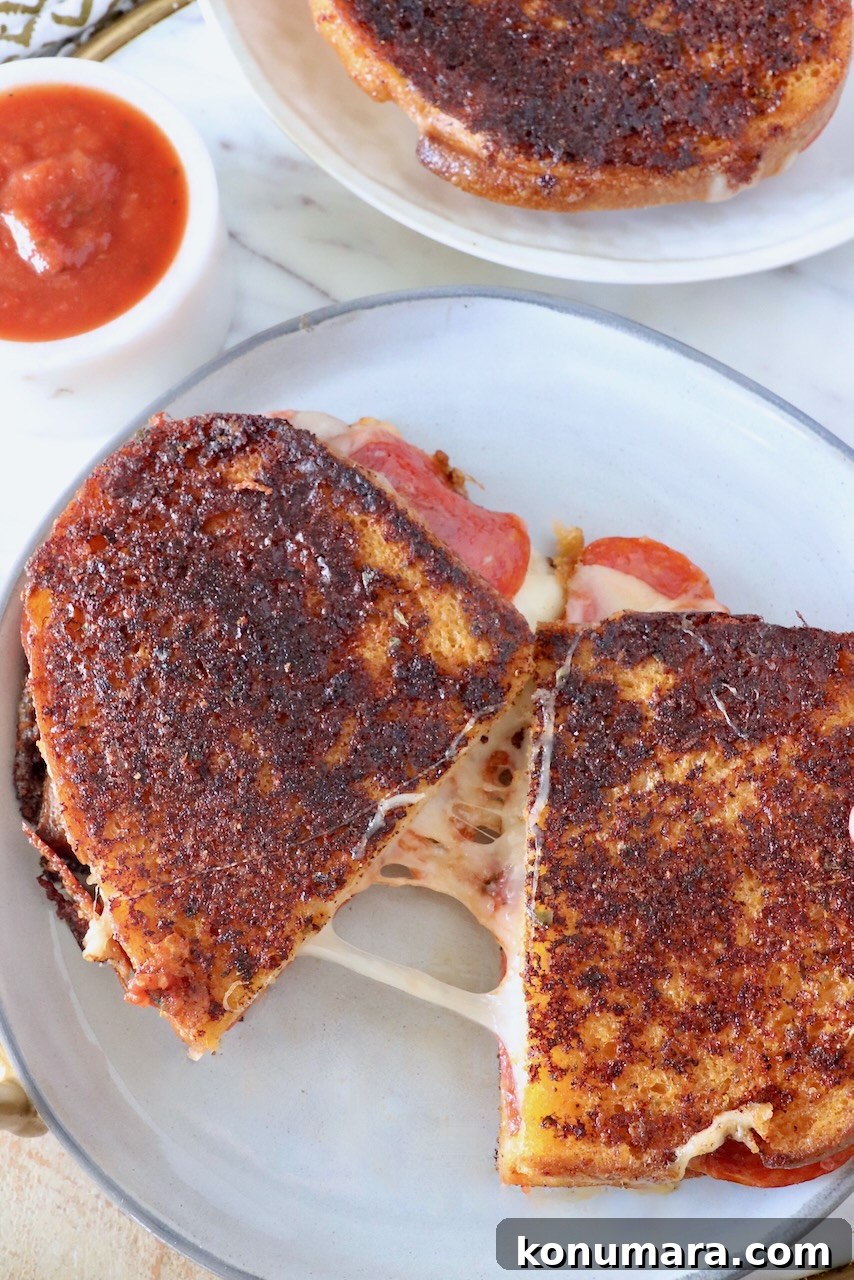 Pepperoni Pizza Grilled Cheese Recipe 11 pizza grilled cheese sandwich cut in half and pulled apart on a plate next to a small bowl of pizza sauce