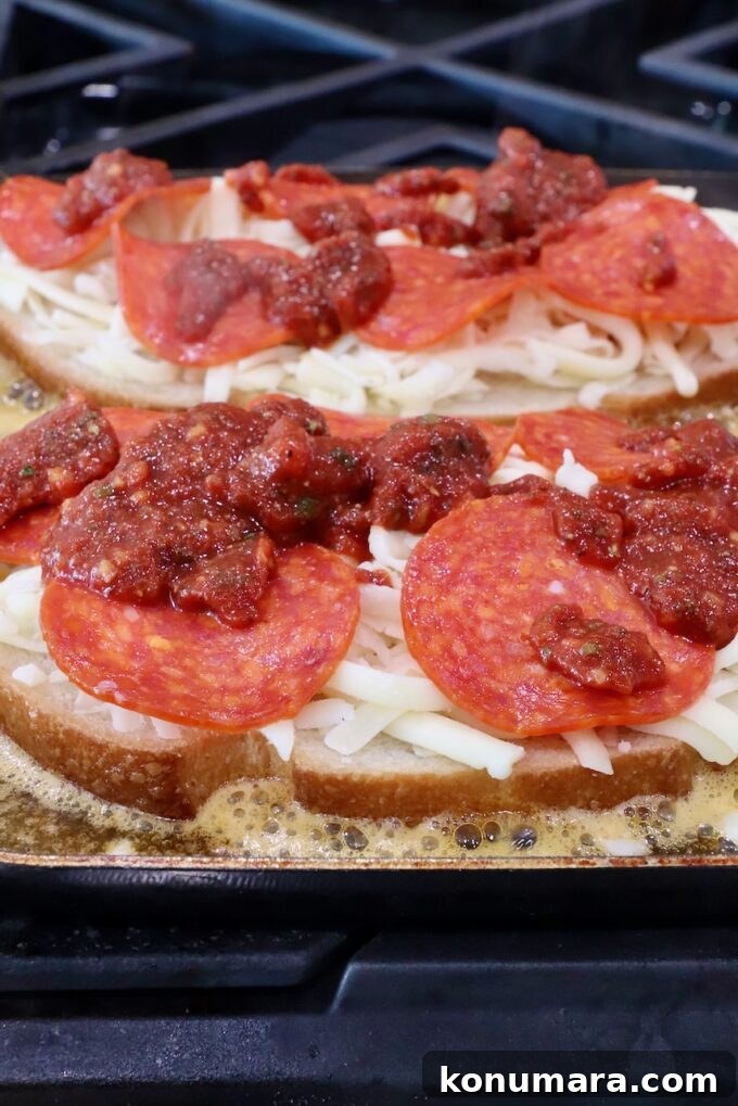 Pepperoni Pizza Grilled Cheese Recipe 7 sliced bread on a skillet topped with cheese, pepperonis and pizza sauce