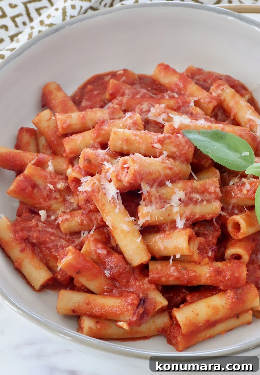 ziti pasta tossed with tomato sauce in a bowl with fresh basil leaves