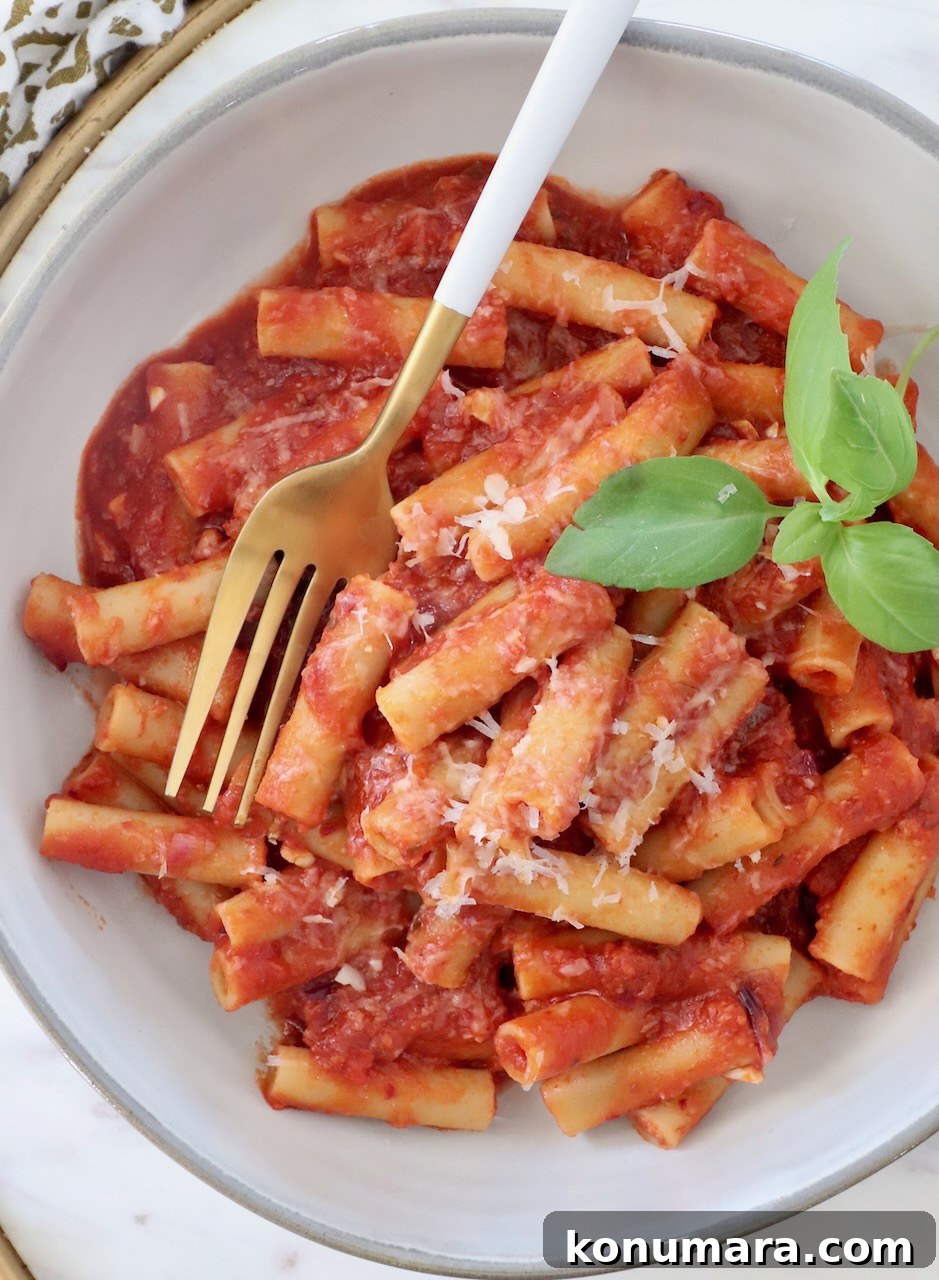 cooked ziti tossed with tomato sauce in a bowl with fresh basil leaves and a fork