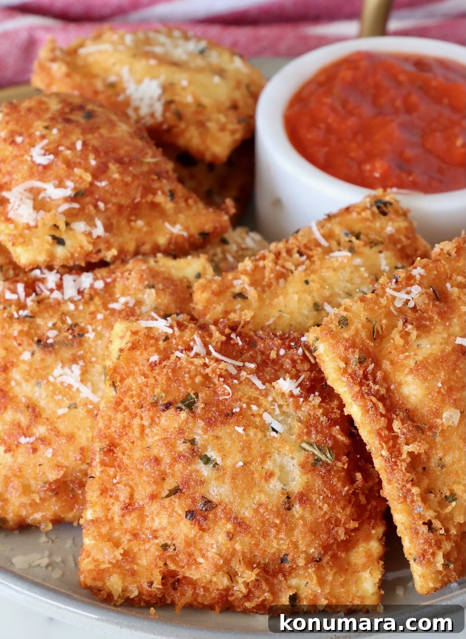 toasted raviolis stacked up on a plate with a bowl of marinara sauce behind them