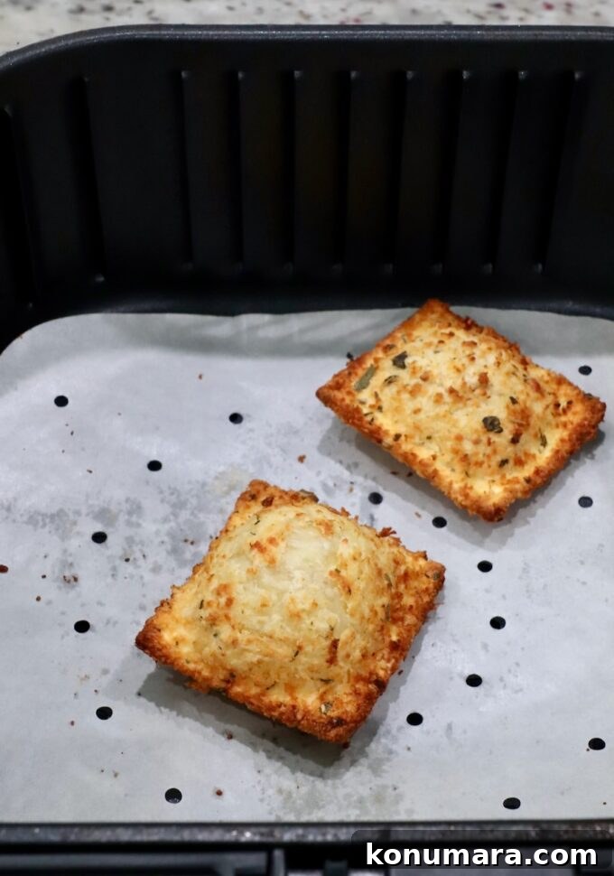two toasted raviolis in an air fryer basket with a parchment paper liner