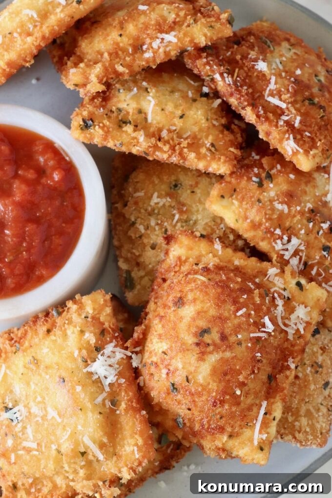toasted raviolis stacked up on a plate with a small bowl of marinara sauce on the side