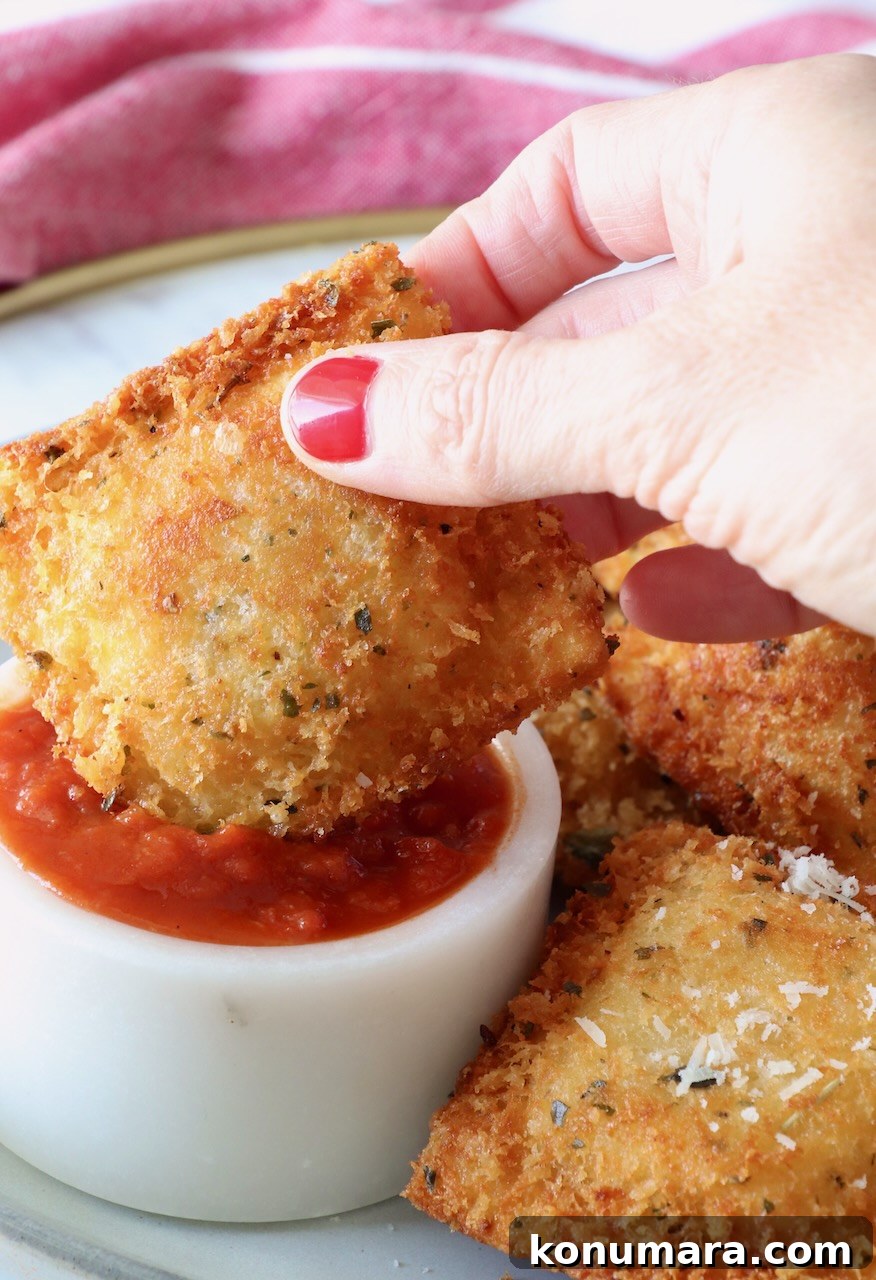 hand holding a toasted ravioli dipped into a small bowl of marinara sauce