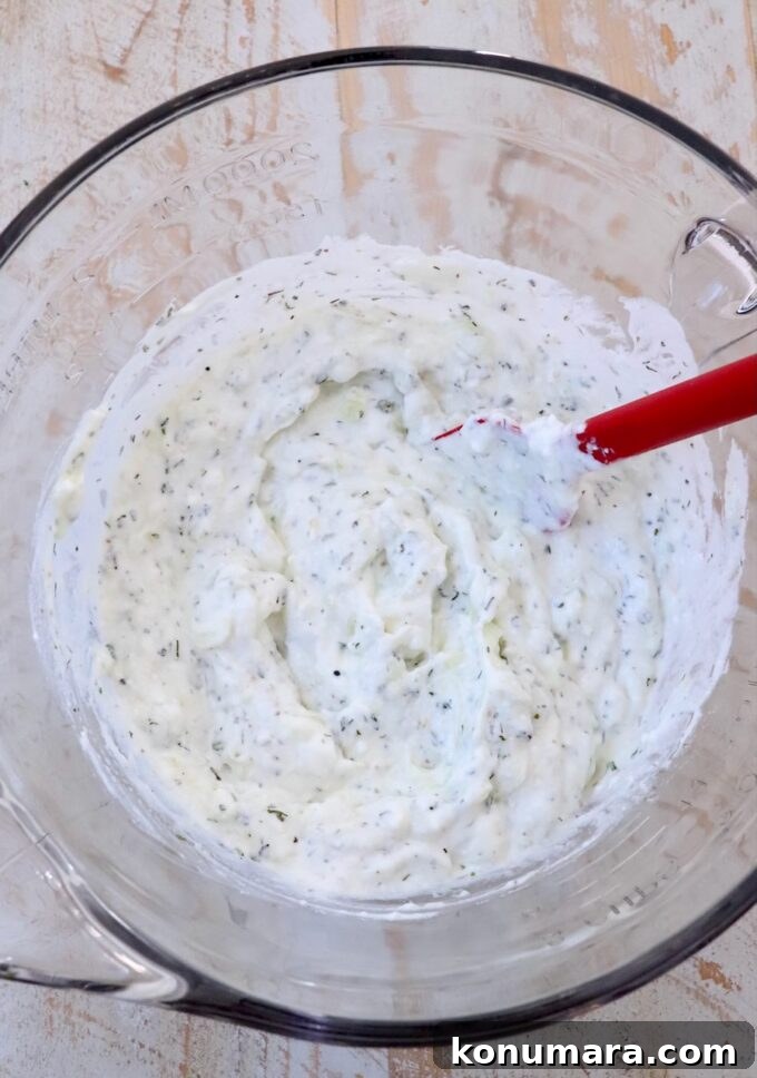 tzatziki sauce mixed up in a large glass bowl with a red spatula