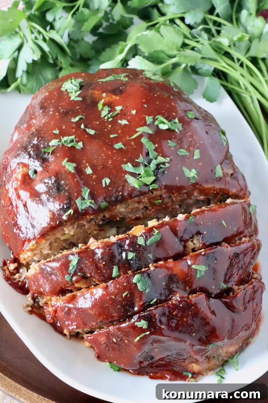 30-Minute Air Fryer Meatloaf Recipe with Crispy Edges 2 glazed, cooked meatloaf, partially sliced on a plate with fresh parsley