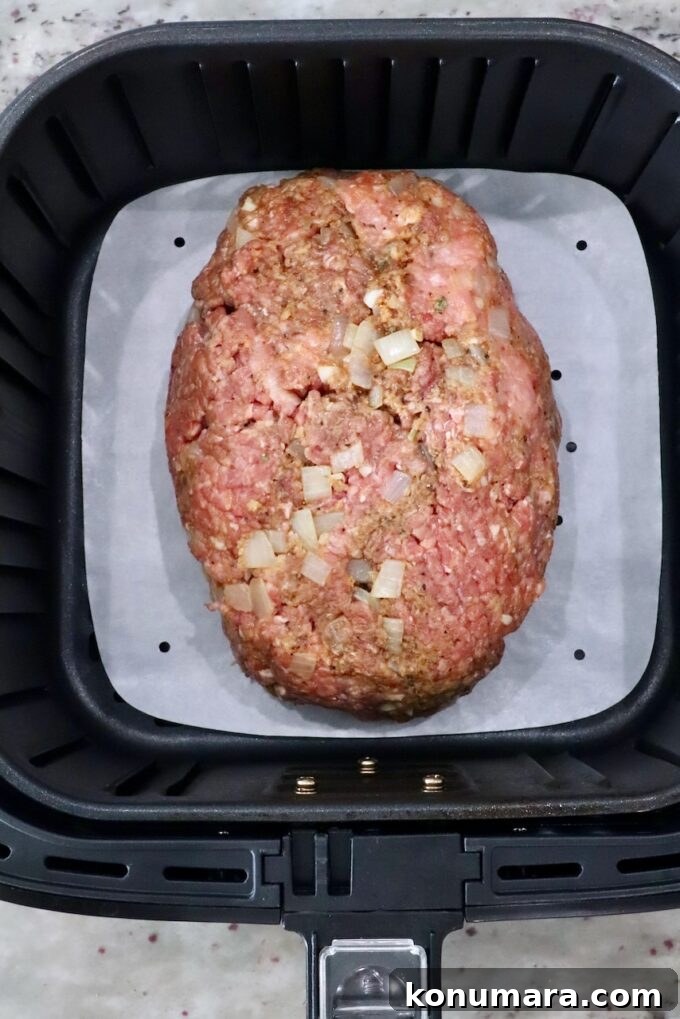 30-Minute Air Fryer Meatloaf Recipe with Crispy Edges 6 uncooked meatloaf in an air fryer basket with a parchment paper liner