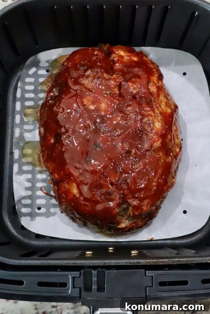 30-Minute Air Fryer Meatloaf Recipe with Crispy Edges 8 cooked, glazed meatloaf in an air fryer basket with a parchment paper liner