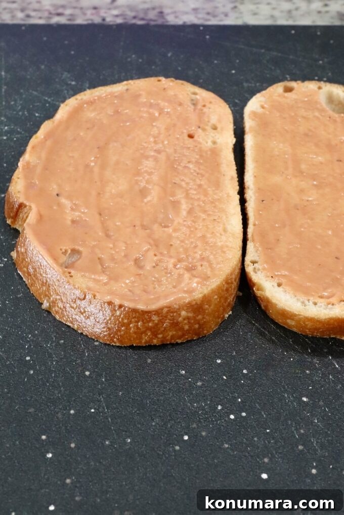 How to Make a Classic Meatloaf Sandwich 4 bbq mayonnaise spread on two slices of bread on a cutting board