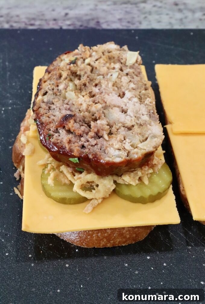How to Make a Classic Meatloaf Sandwich 7 slice of meatloaf on top of cheese, pickles, and fried onion strings, on a piece of bread