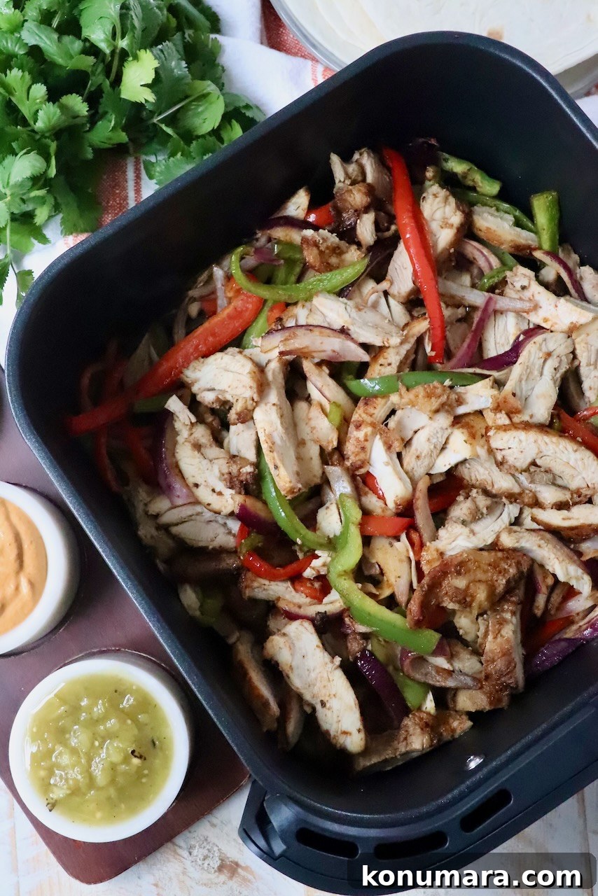 cooked sliced chicken, bell peppers, and onions in an air fryer basket
