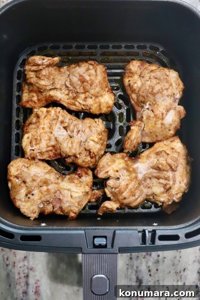 seasoned, cooked chicken thighs in an air fryer basket