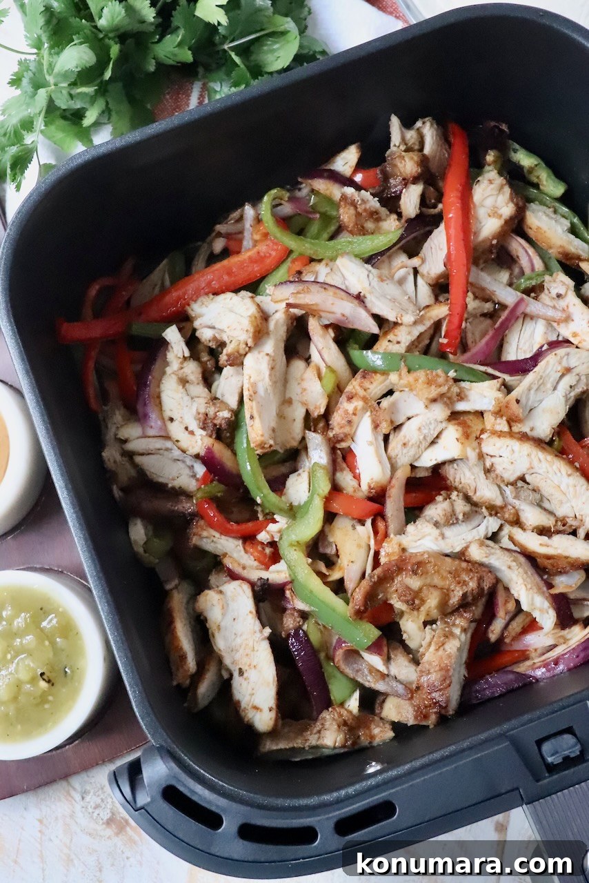 cooked, sliced fajita chicken thighs and vegetables in an air fryer basket