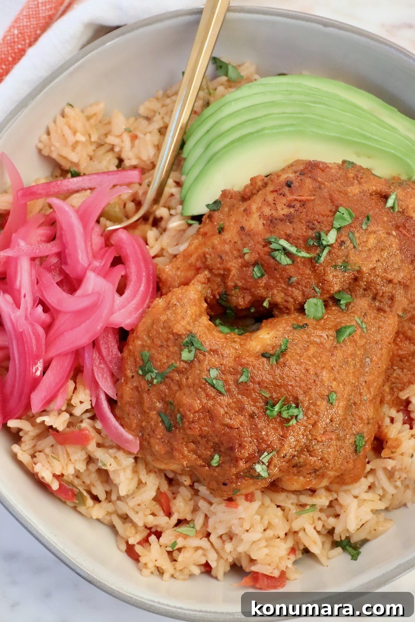 adobo chicken on top of Mexican rice in a bowl with a fork, pickled onions and avocado slices