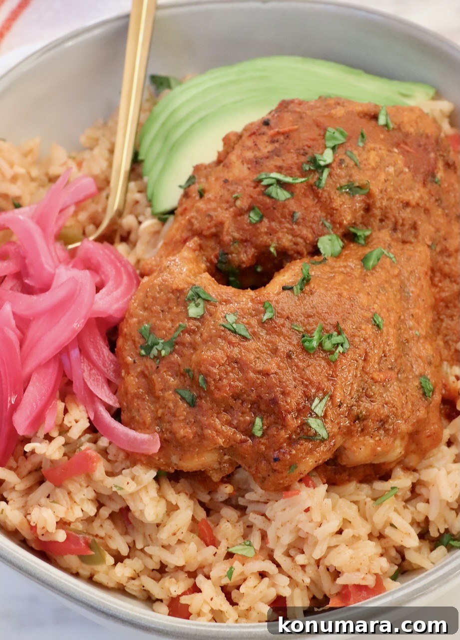 Classic Mexican Chicken Adobo Recipe 2 adobo chicken on top of Mexican rice in a bowl with sliced avocado, pickled onions and a gold fork
