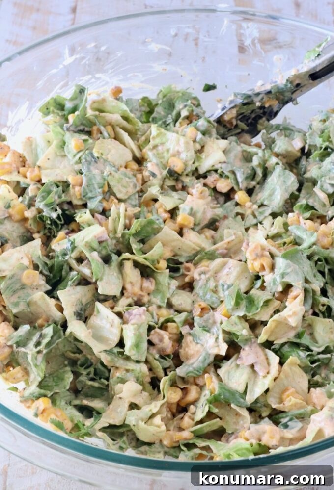 tossed street corn salad in a large glass bowl with kitchen tongs