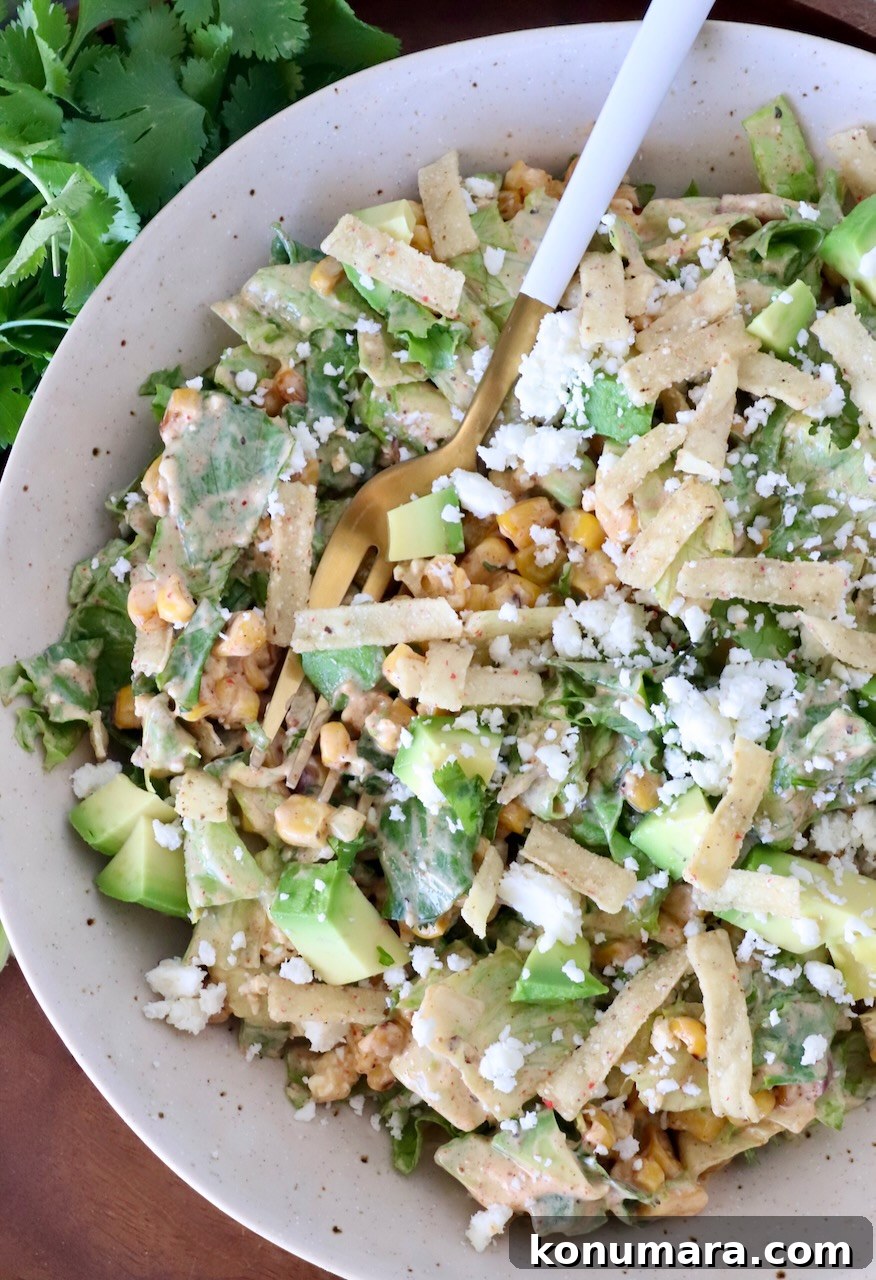 street corn salad in a bowl with a fork, topped with tortilla strips