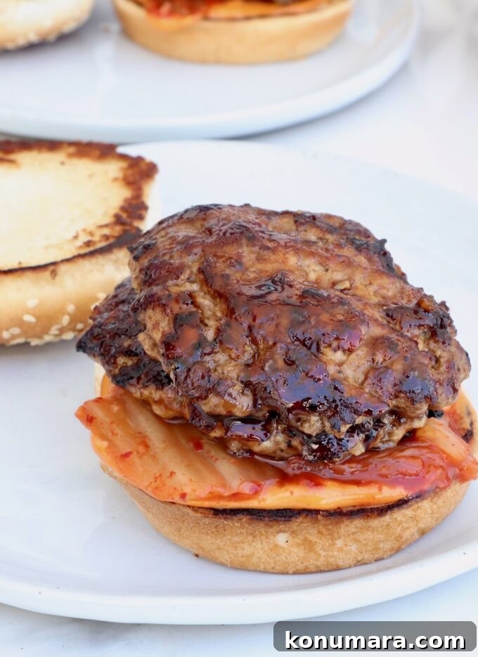 Korean BBQ Burger with Gochujang Glaze and Kimchi Slaw 9 hamburger bun on a plate topped with kimchi and bbq glazed burger patties