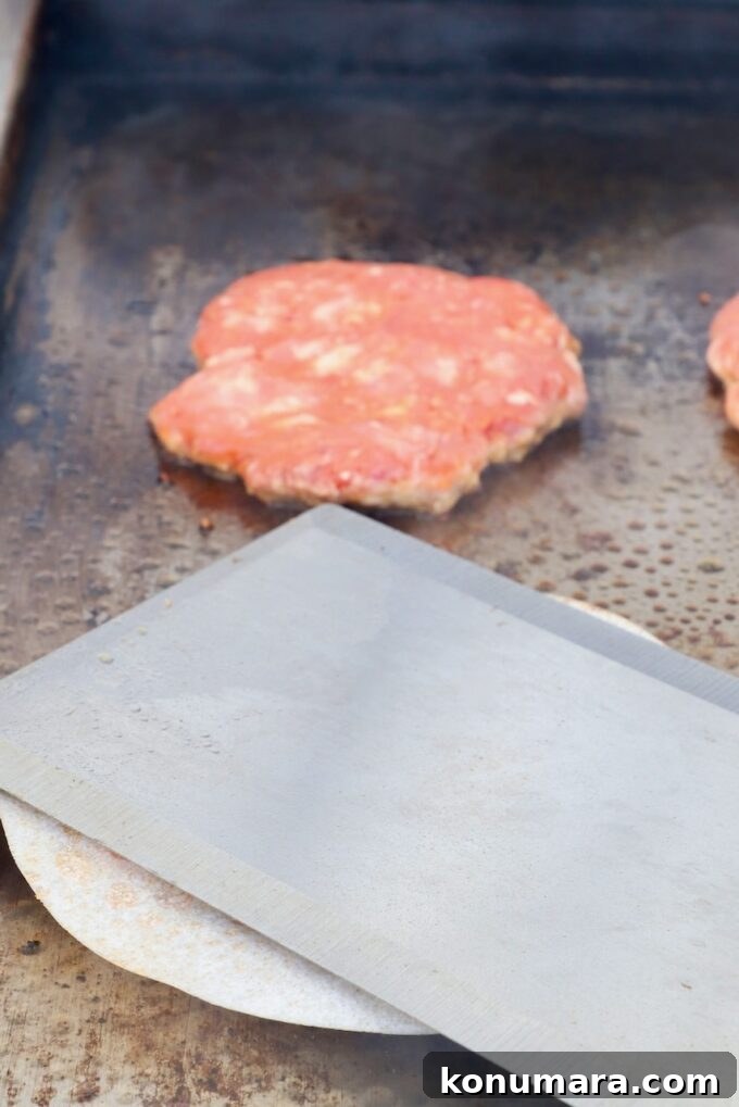 Korean BBQ Burger with Gochujang Glaze and Kimchi Slaw 6 burger patty smashed with a large metal spatula on a griddle