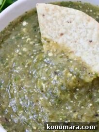 tomatillo salsa in a bowl with a hand dipping a tortilla chip in the salsa