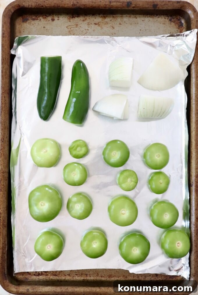 fresh tomatillos, white onion and jalapenos on a piece of foil on a baking sheet