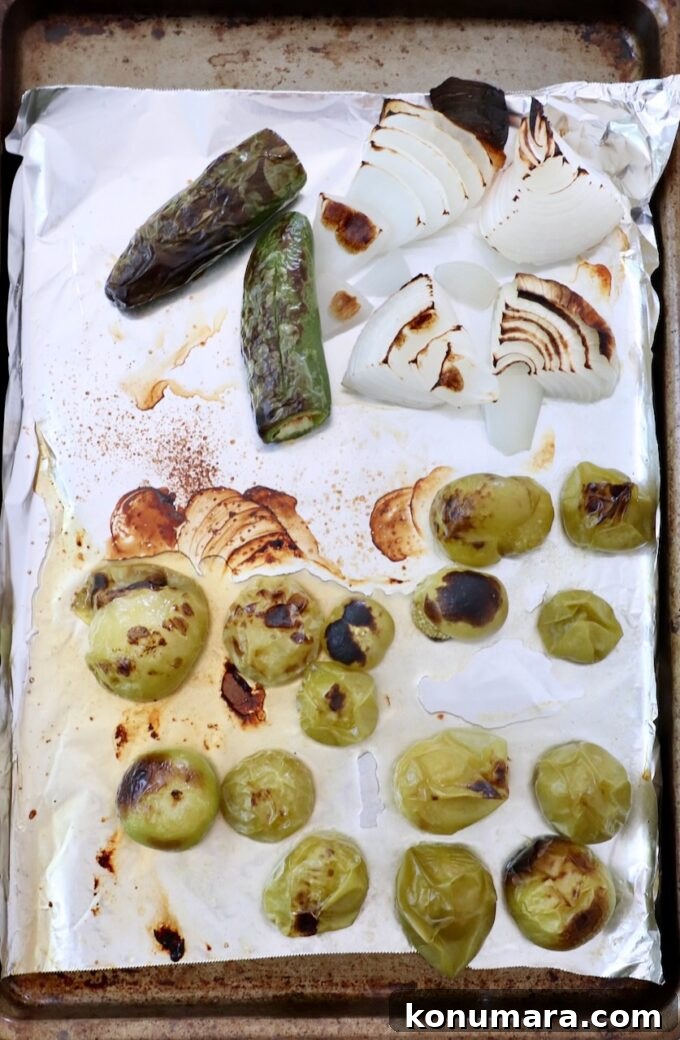 roasted tomatillos, white onion and jalapenos on a piece of foil on a baking sheet