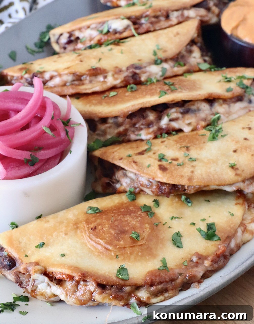 Smoky Black Bean Tacos with Avocado Lime Crema 7 crispy black bean tacos stacked up on a plate with a side of pickled red onions